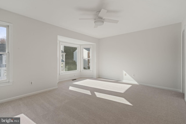 carpeted empty room featuring visible vents, a ceiling fan, and baseboards