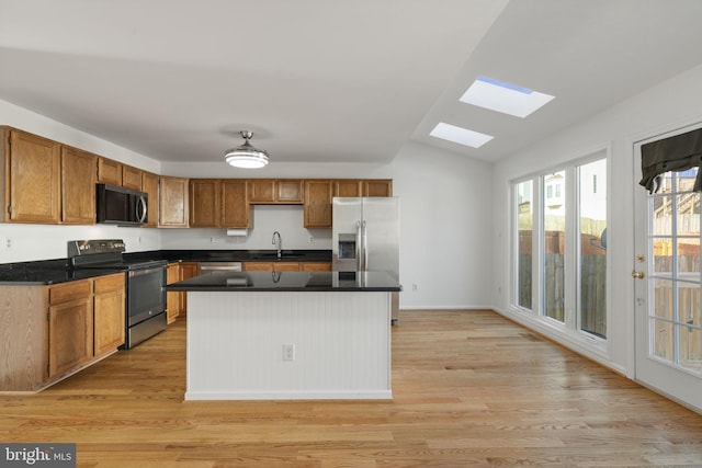 kitchen featuring light wood-style floors, appliances with stainless steel finishes, lofted ceiling with skylight, dark countertops, and a center island