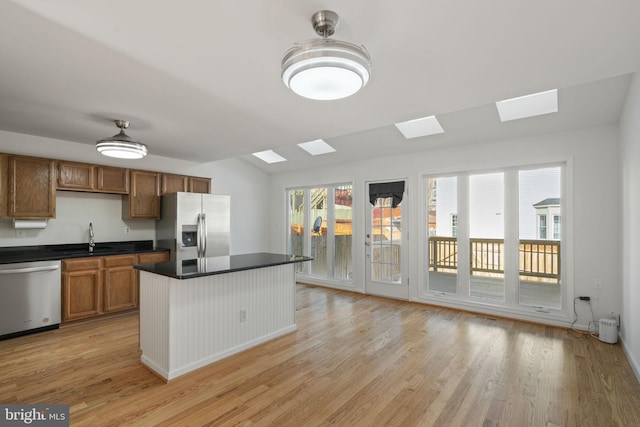 kitchen with a sink, dark countertops, stainless steel appliances, a skylight, and light wood finished floors