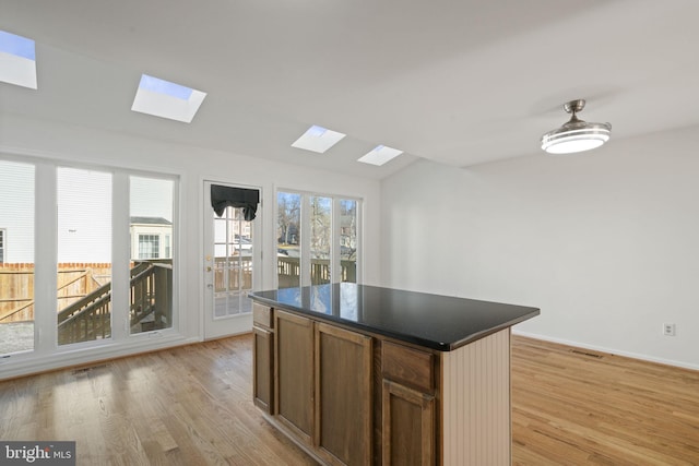 kitchen with dark countertops, visible vents, a kitchen island, and light wood-type flooring