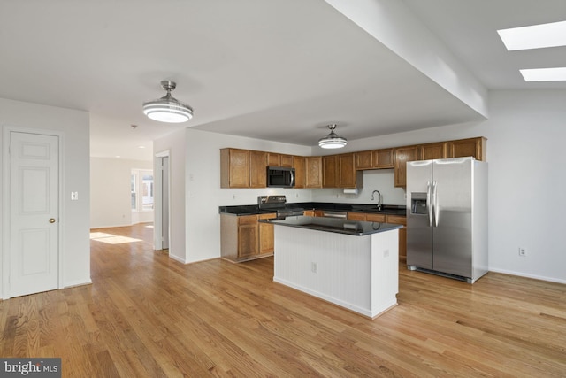 kitchen with dark countertops, light wood-style flooring, appliances with stainless steel finishes, a skylight, and brown cabinetry