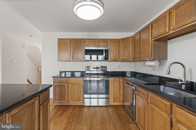 kitchen featuring a sink, dark stone countertops, stainless steel appliances, brown cabinetry, and dark wood-style flooring