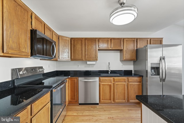 kitchen featuring a sink, stainless steel appliances, dark stone counters, brown cabinetry, and light wood finished floors