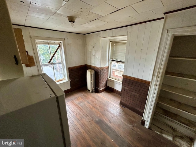 interior space featuring wooden walls, radiator heating unit, crown molding, and wood finished floors