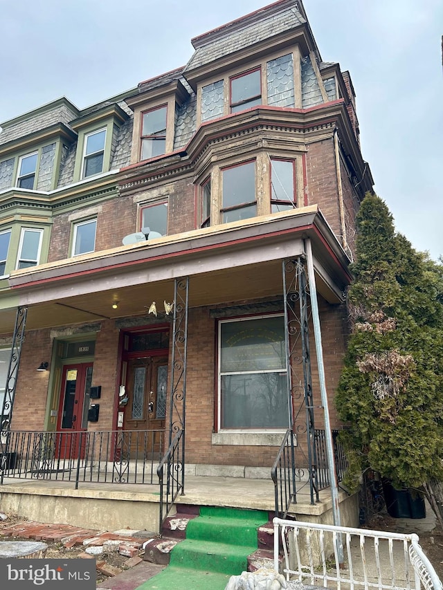 view of front of property with a porch, mansard roof, and brick siding