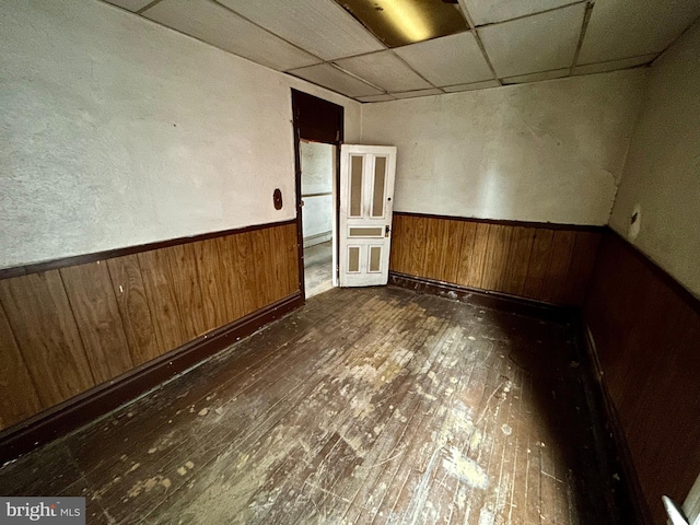 spare room featuring a paneled ceiling, a wainscoted wall, wooden walls, and dark wood-style flooring