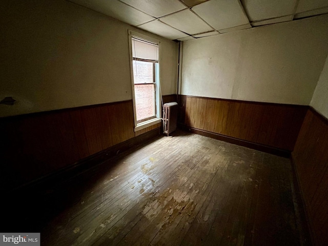 spare room with radiator, a wainscoted wall, wood walls, and wood finished floors