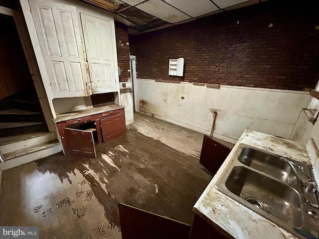 kitchen with brick wall, light countertops, wainscoting, and a sink