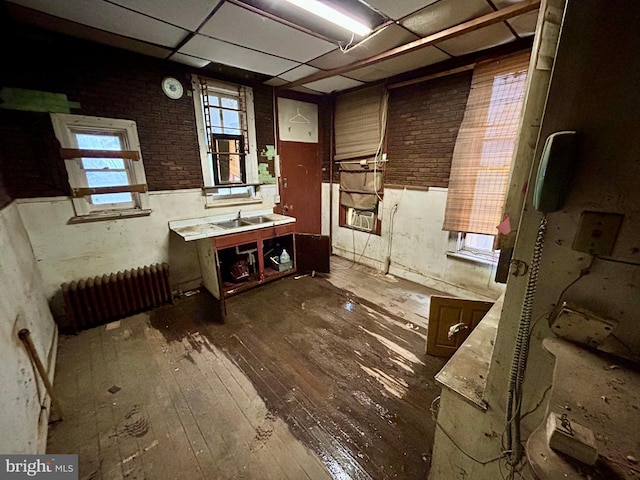 bathroom with brick wall, radiator heating unit, a drop ceiling, and wood finished floors