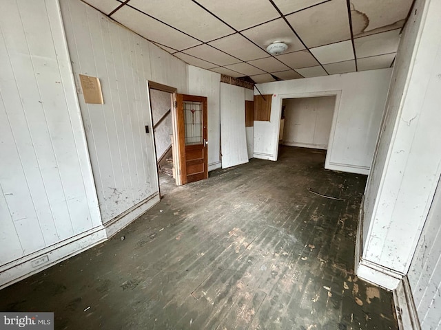 empty room featuring a paneled ceiling, dark wood-style floors, and wooden walls