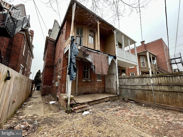 view of side of property featuring brick siding, fence, and a balcony