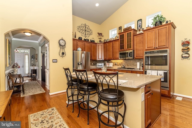 kitchen with arched walkways, a breakfast bar area, stainless steel appliances, crown molding, and high vaulted ceiling