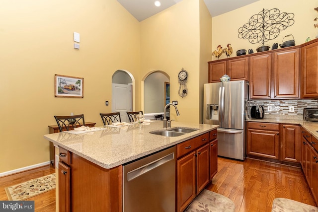 kitchen featuring light stone counters, appliances with stainless steel finishes, dark wood-type flooring, a kitchen island with sink, and a sink