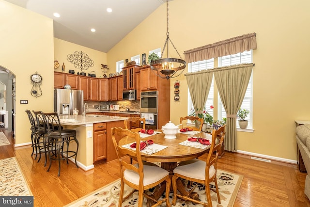 dining area featuring light wood-style floors, baseboards, and high vaulted ceiling