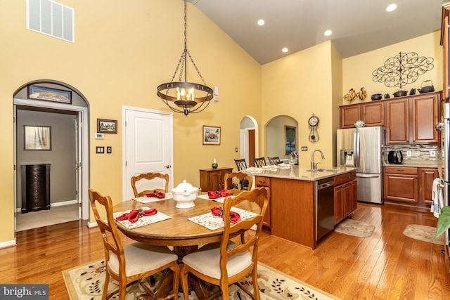 dining space with arched walkways, a chandelier, visible vents, light wood-style flooring, and high vaulted ceiling