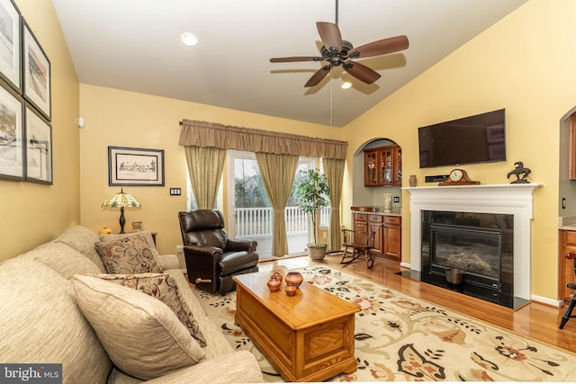 living room featuring a ceiling fan, a glass covered fireplace, vaulted ceiling, and wood finished floors