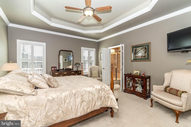 bedroom with light colored carpet, a ceiling fan, ornamental molding, a raised ceiling, and ensuite bath