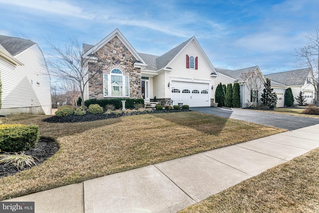 traditional home with an attached garage, driveway, stone siding, and a front yard