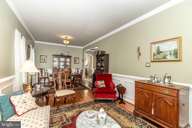 living area with arched walkways, a decorative wall, wood finished floors, ornamental molding, and wainscoting