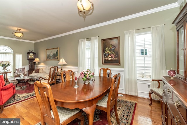 dining room with plenty of natural light, crown molding, wood finished floors, and wainscoting