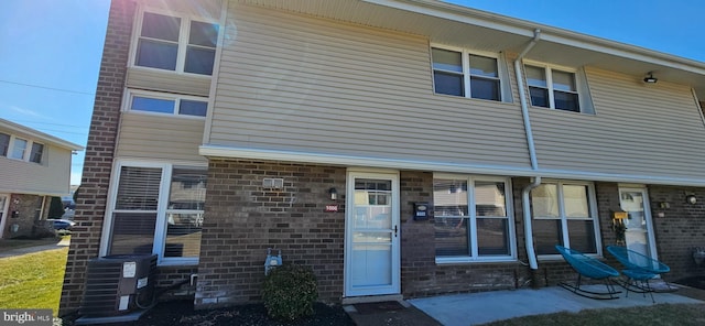 view of front of home with brick siding, a patio, and central AC unit