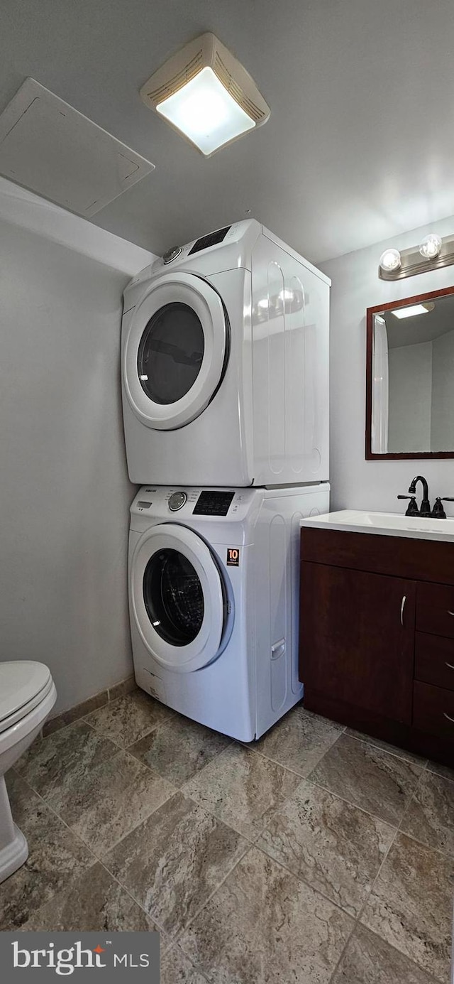 laundry area with stacked washer and dryer, laundry area, a sink, baseboards, and stone finish floor