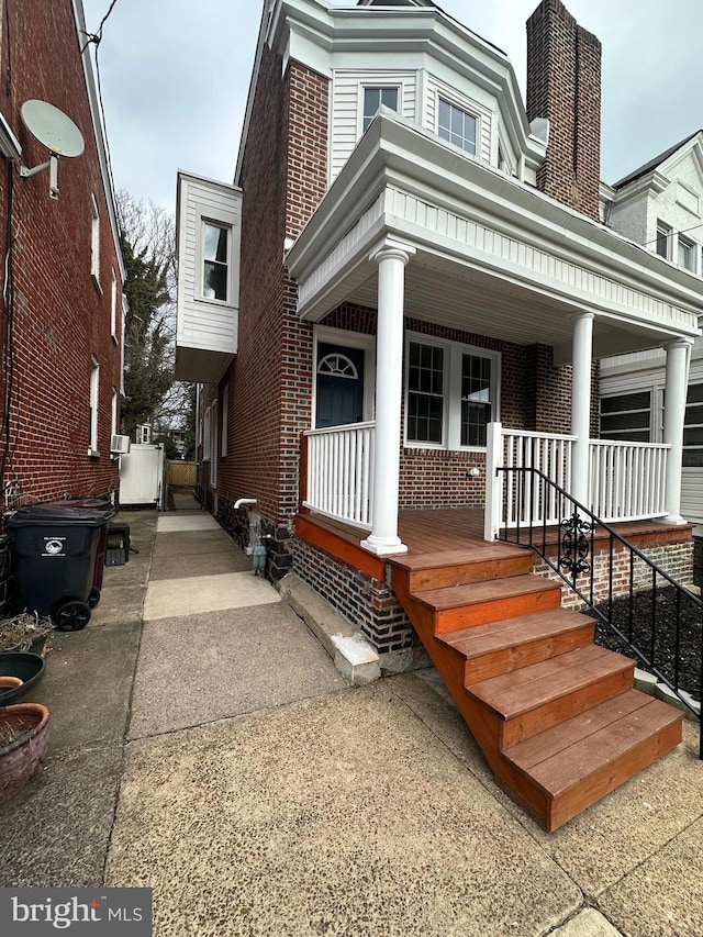 view of front of house with a porch, brick siding, and a chimney