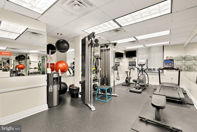 exercise room featuring a paneled ceiling, visible vents, and baseboards