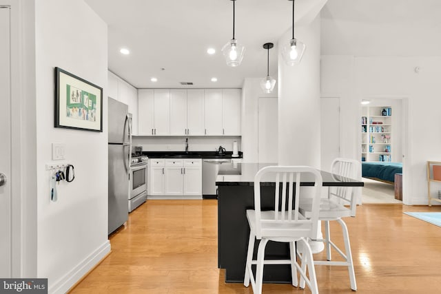 kitchen with a breakfast bar, light wood-style flooring, appliances with stainless steel finishes, white cabinetry, and dark countertops