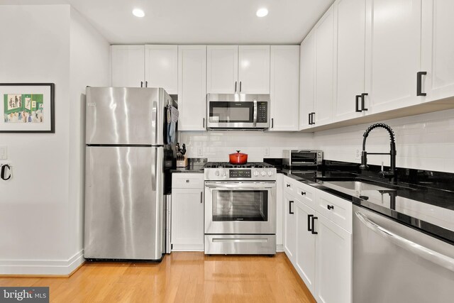 kitchen with a sink, tasteful backsplash, white cabinetry, appliances with stainless steel finishes, and light wood finished floors