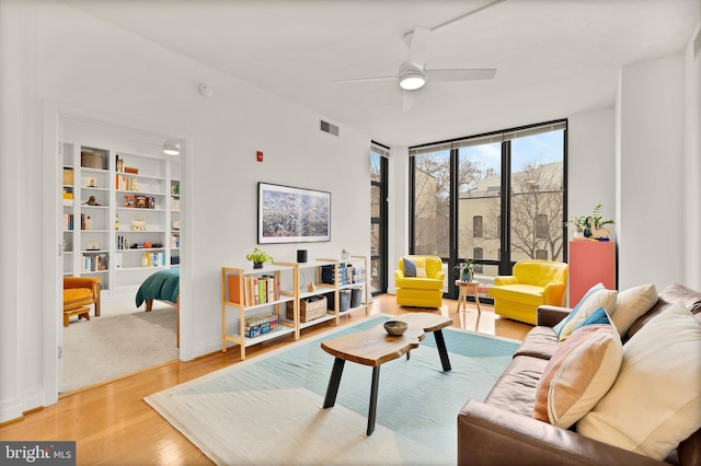 living area featuring a ceiling fan, floor to ceiling windows, wood finished floors, and visible vents