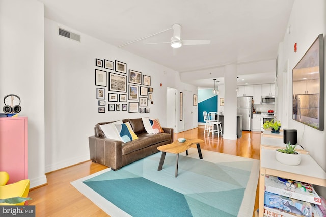 living room featuring baseboards, visible vents, light wood finished floors, and ceiling fan