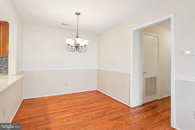 unfurnished dining area featuring baseboards, wood finished floors, visible vents, and a chandelier