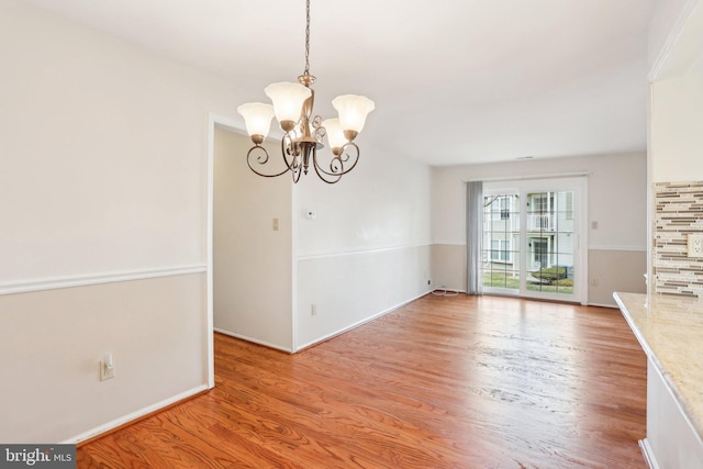 unfurnished dining area with baseboards, light wood-type flooring, and an inviting chandelier