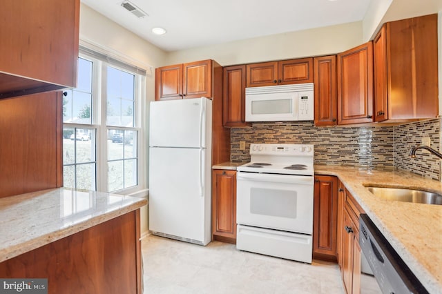 kitchen with brown cabinetry, visible vents, white appliances, and a sink