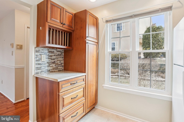 kitchen with light countertops, tasteful backsplash, a wealth of natural light, and brown cabinets