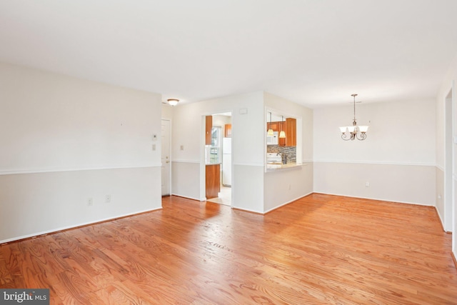 spare room featuring light wood finished floors and a notable chandelier