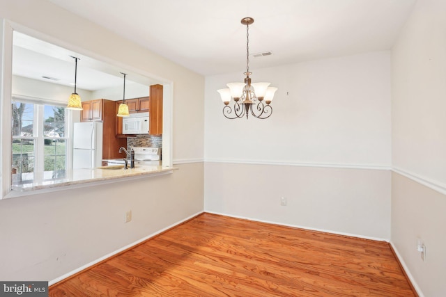 unfurnished dining area featuring light wood finished floors, visible vents, baseboards, a notable chandelier, and a sink