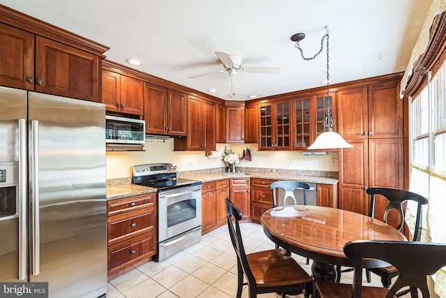 kitchen featuring light stone counters, pendant lighting, light tile patterned floors, appliances with stainless steel finishes, and glass insert cabinets