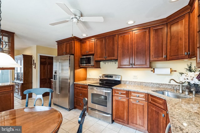 kitchen with light tile patterned floors, ceiling fan, light stone counters, stainless steel appliances, and a sink