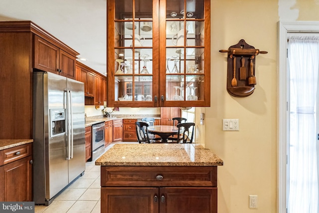 kitchen with appliances with stainless steel finishes, glass insert cabinets, light stone counters, and light tile patterned floors