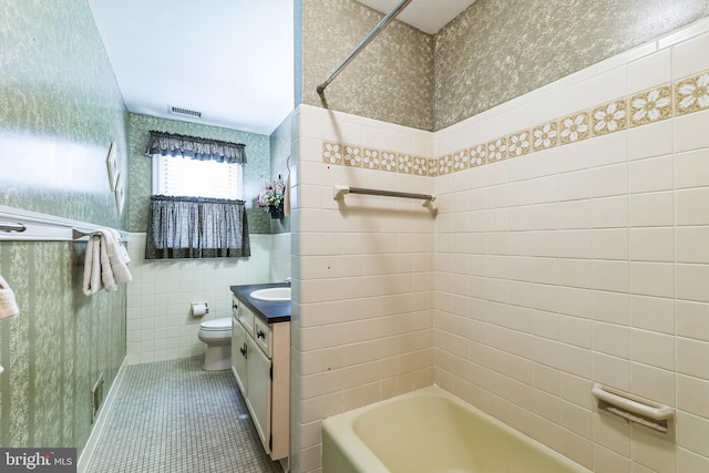 bathroom with wallpapered walls, toilet, tile patterned flooring, vanity, and tile walls