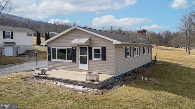 view of front of home with a patio area, a chimney, and a front yard