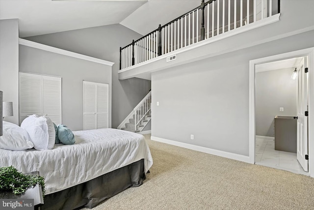 carpeted bedroom featuring ensuite bathroom, high vaulted ceiling, visible vents, baseboards, and two closets