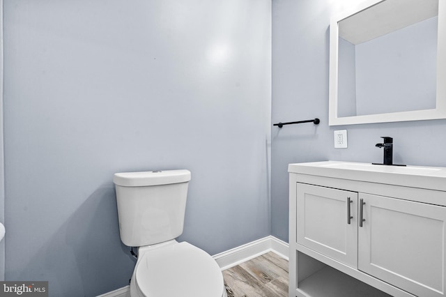 half bathroom featuring vanity, wood finished floors, and toilet