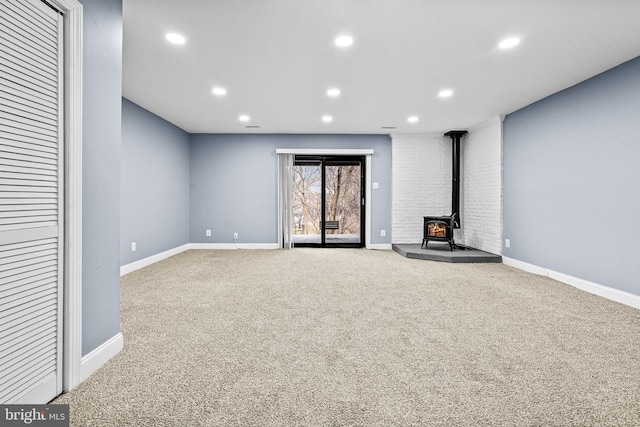 unfurnished living room featuring baseboards, carpet flooring, a wood stove, and recessed lighting