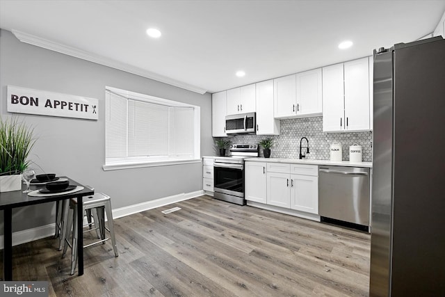 kitchen with white cabinets, appliances with stainless steel finishes, light countertops, light wood-style floors, and backsplash