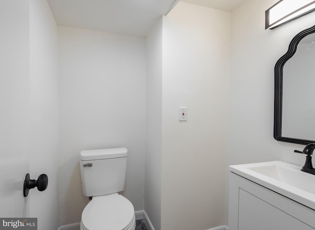 half bath featuring toilet, baseboards, and vanity