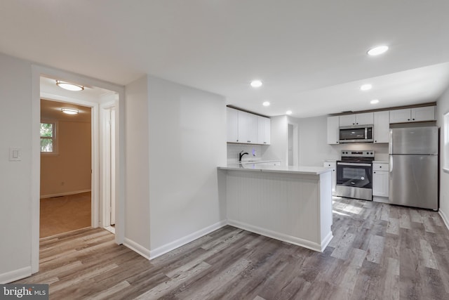 kitchen featuring stainless steel appliances, a peninsula, white cabinets, light countertops, and light wood finished floors