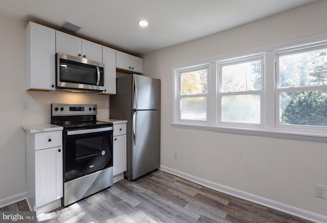 kitchen with baseboards, white cabinets, light countertops, appliances with stainless steel finishes, and light wood-type flooring